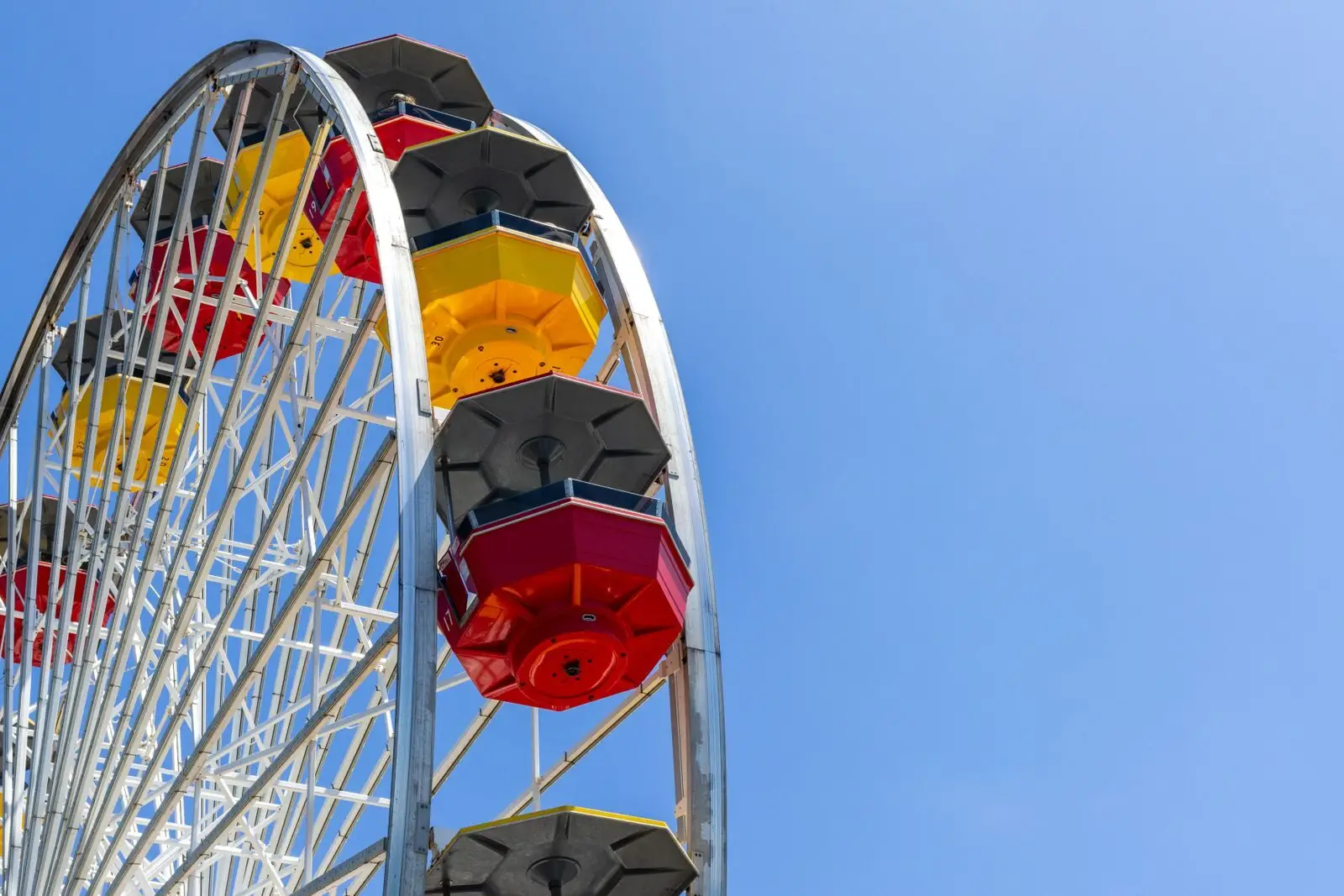 A vibrant ferris wheel with red, yellow, and black gondolas against a bright blue sky.