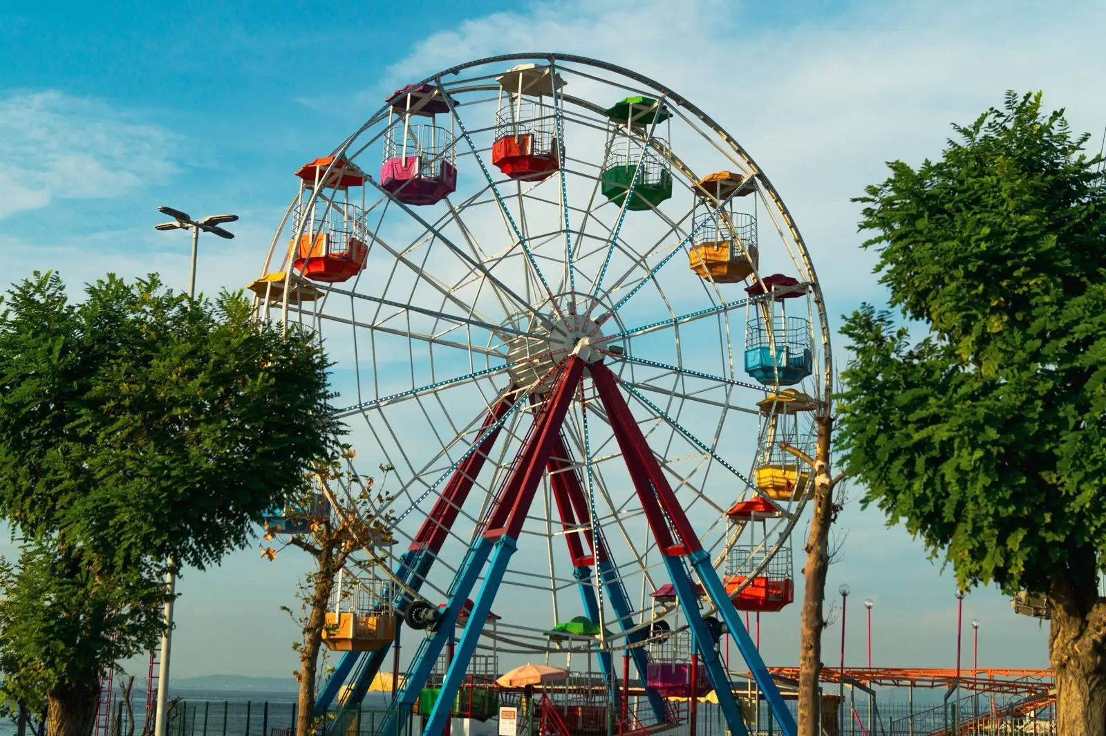 Colorful Ferris wheel at an outdoor amusement park during daytime, surrounded by trees and blue sky.