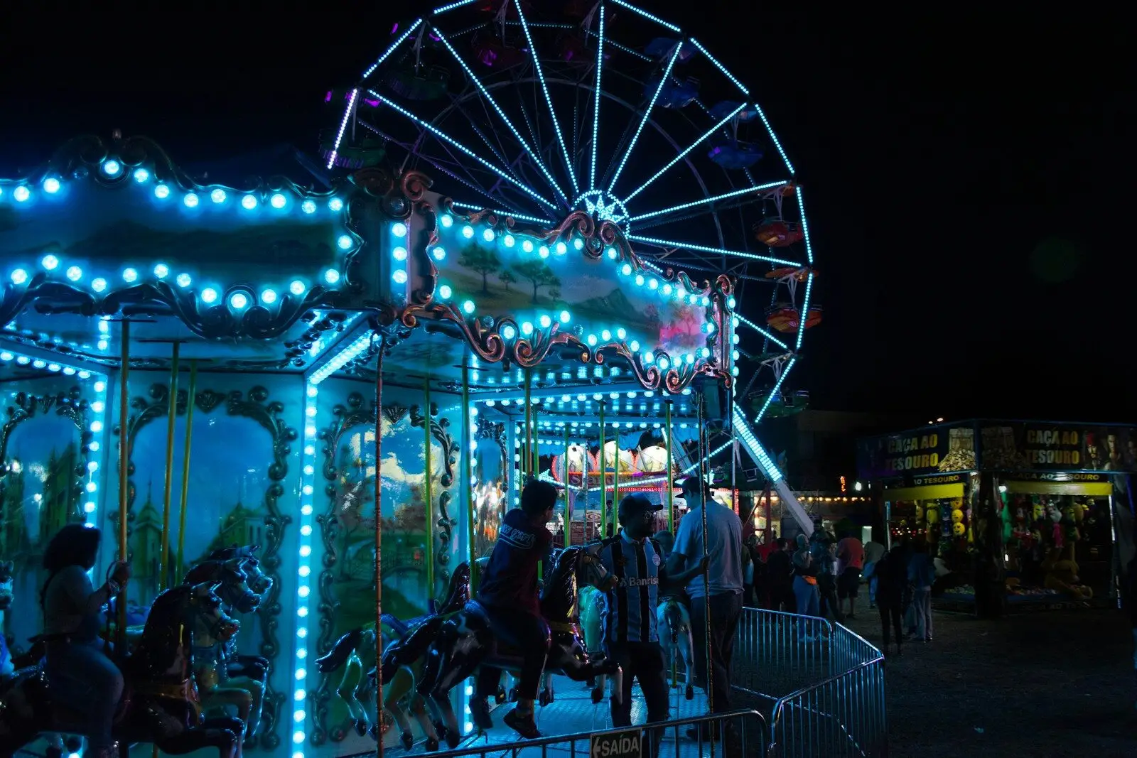 A brightly lit ferris wheel and carousel at night.