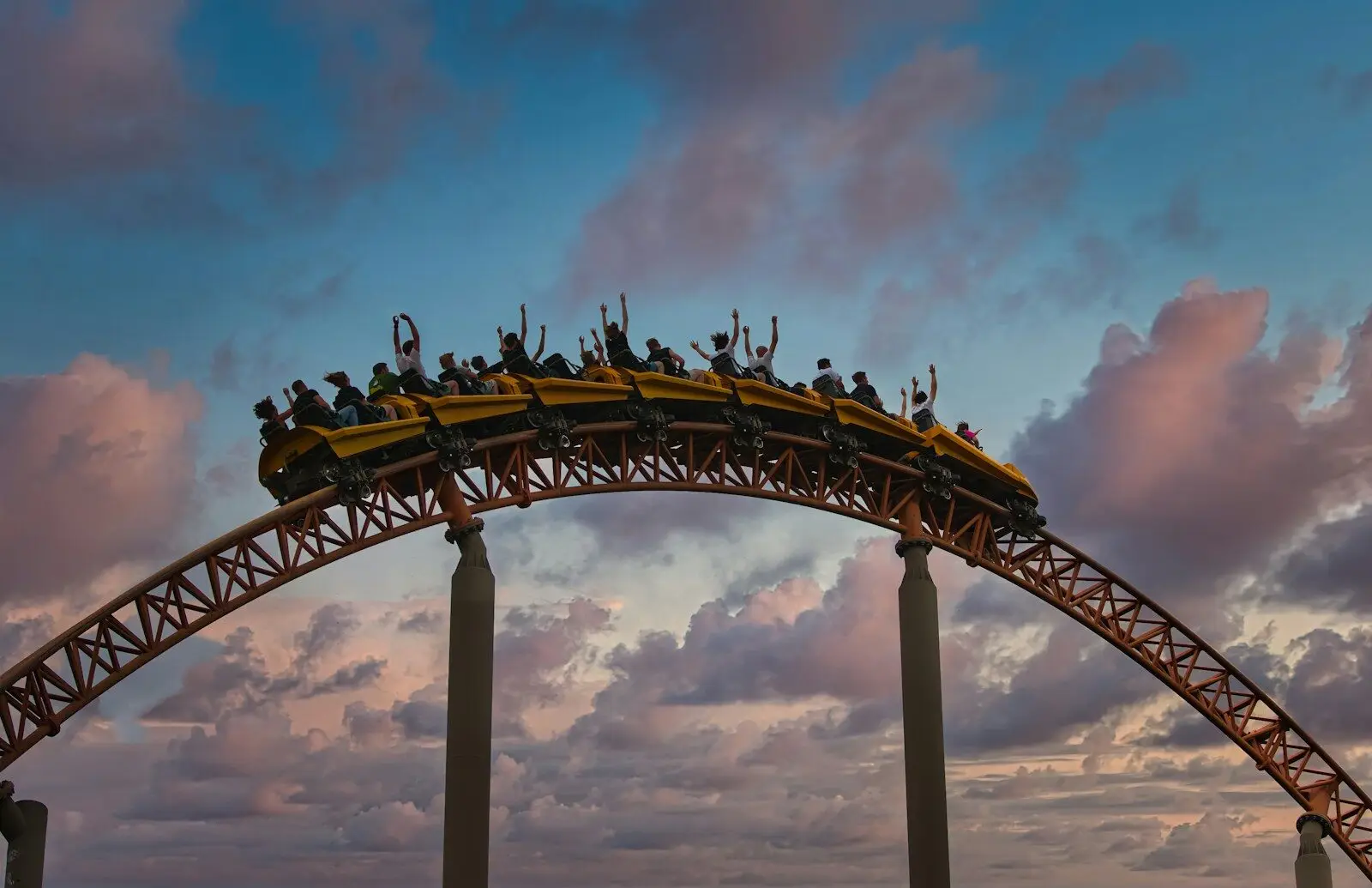 Roller coaster with riders cresting a hill at sunset