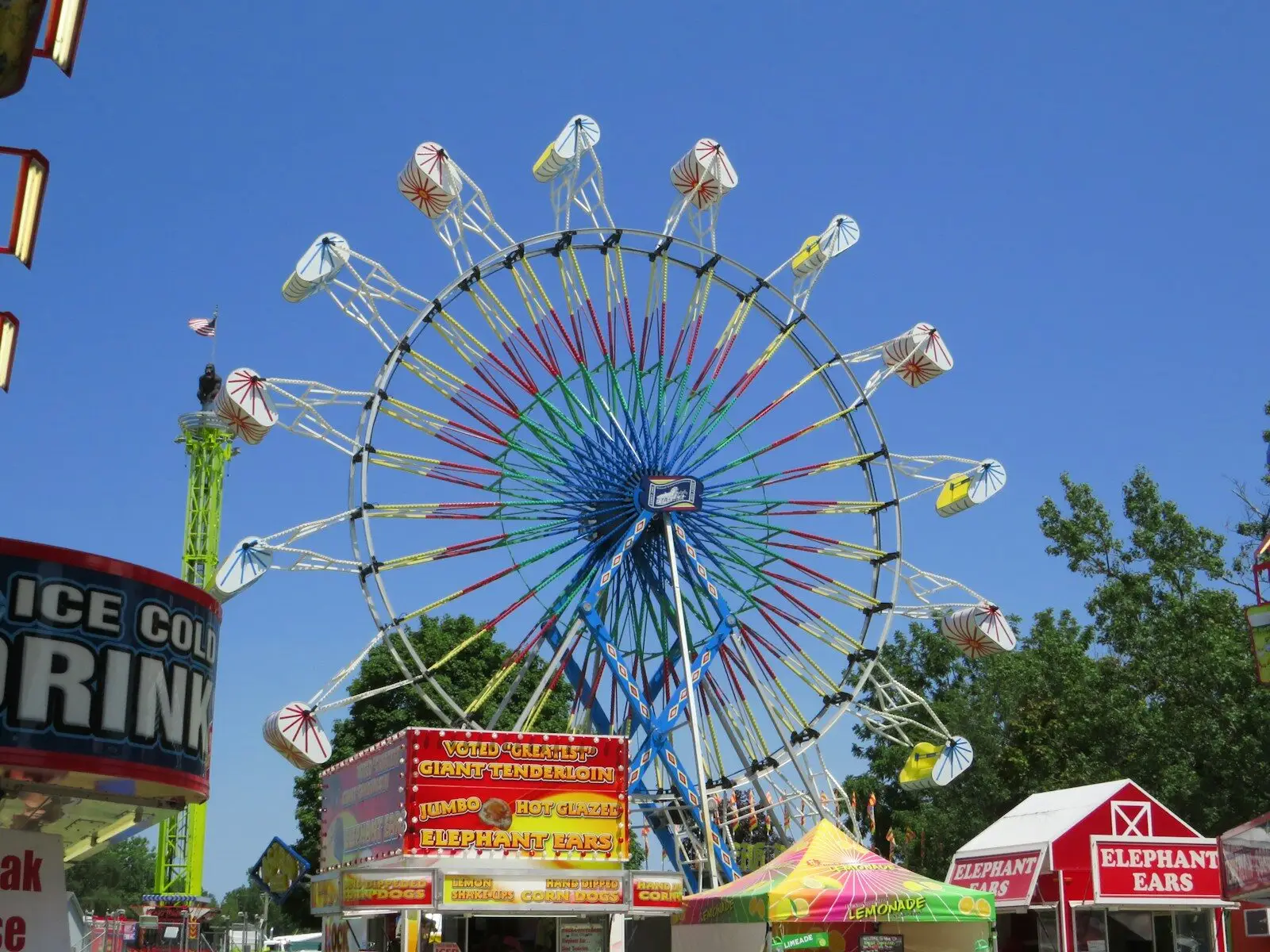 A colorful ferris wheel dominates a sunny fairground scene.