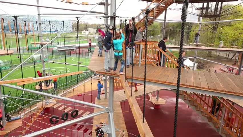 Happy children climbing on a colorful, low-height wooden climbing structure in a sunny playground.