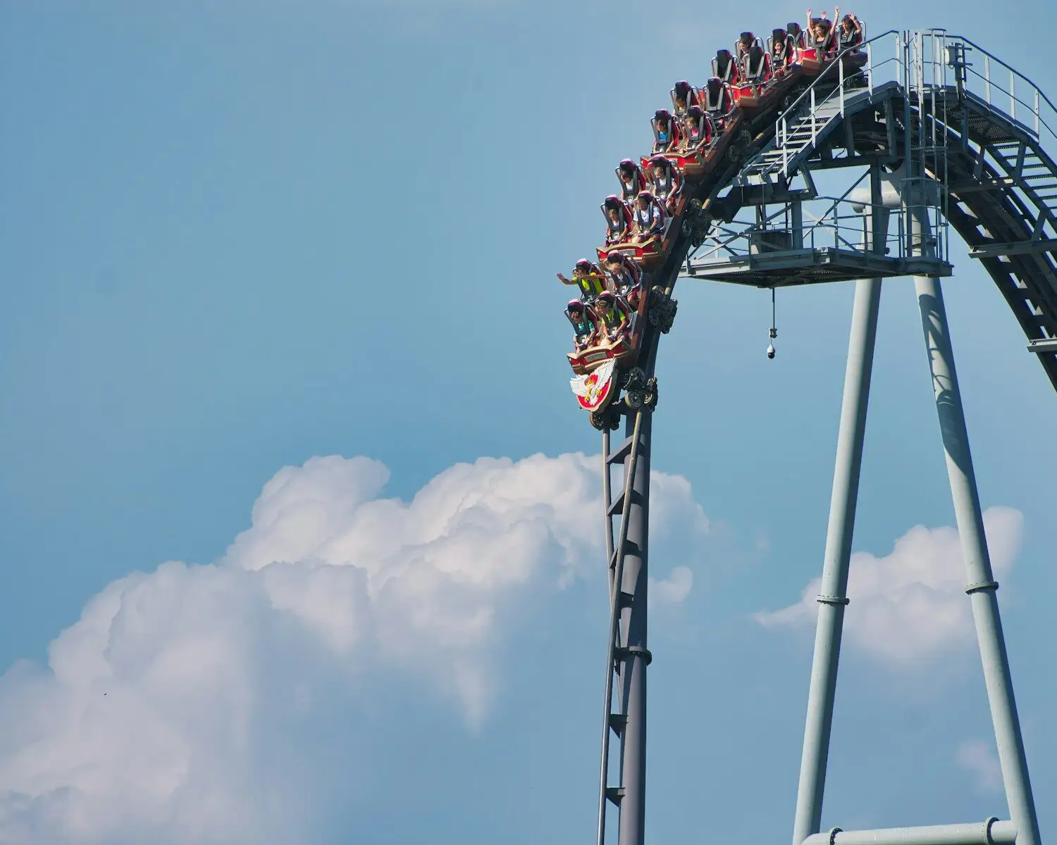 Roller coaster riders descend a steep drop against blue sky.