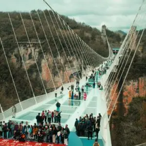 People walk across a modern glass suspension bridge.