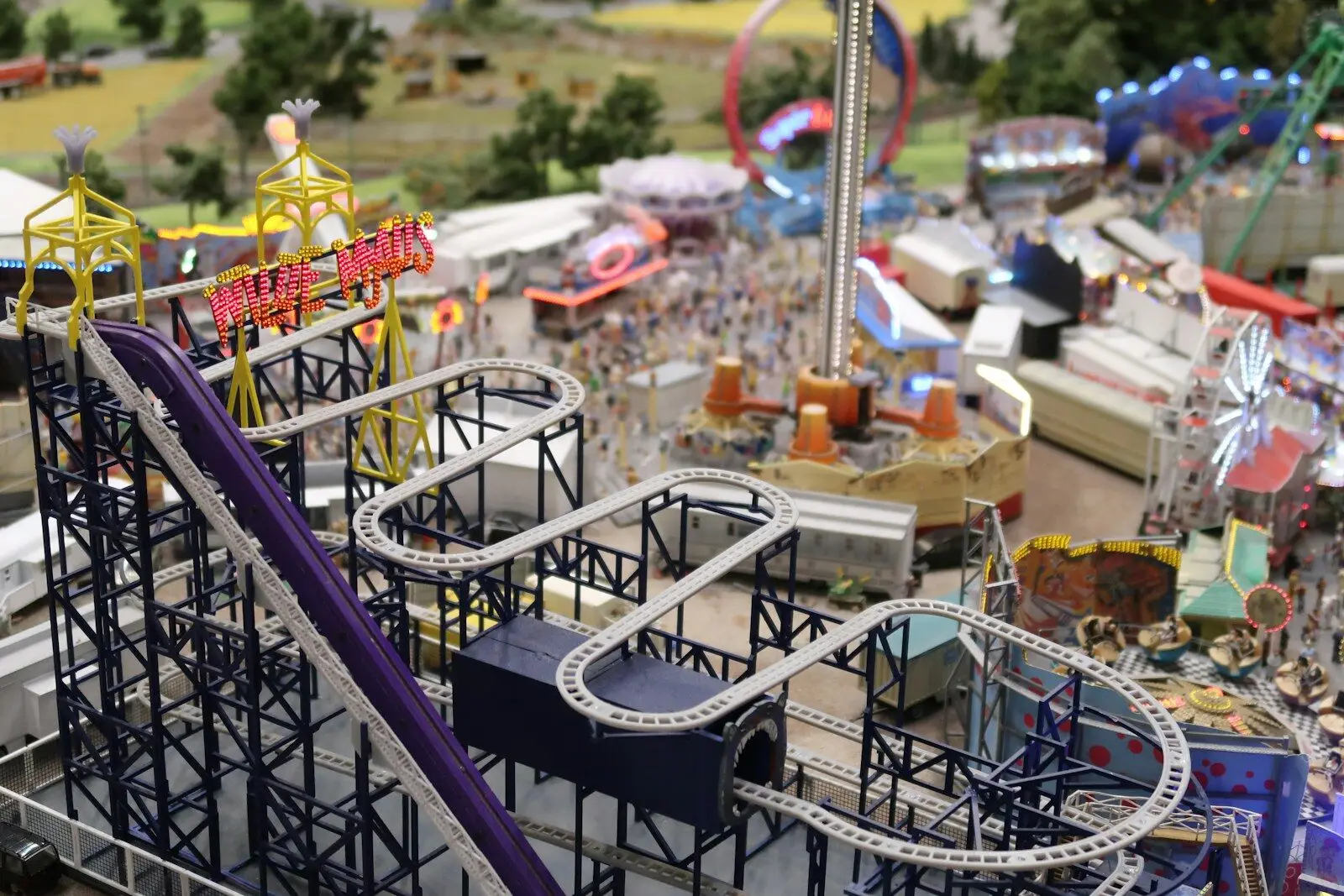 Miniature amusement park with a purple roller coaster and crowds.