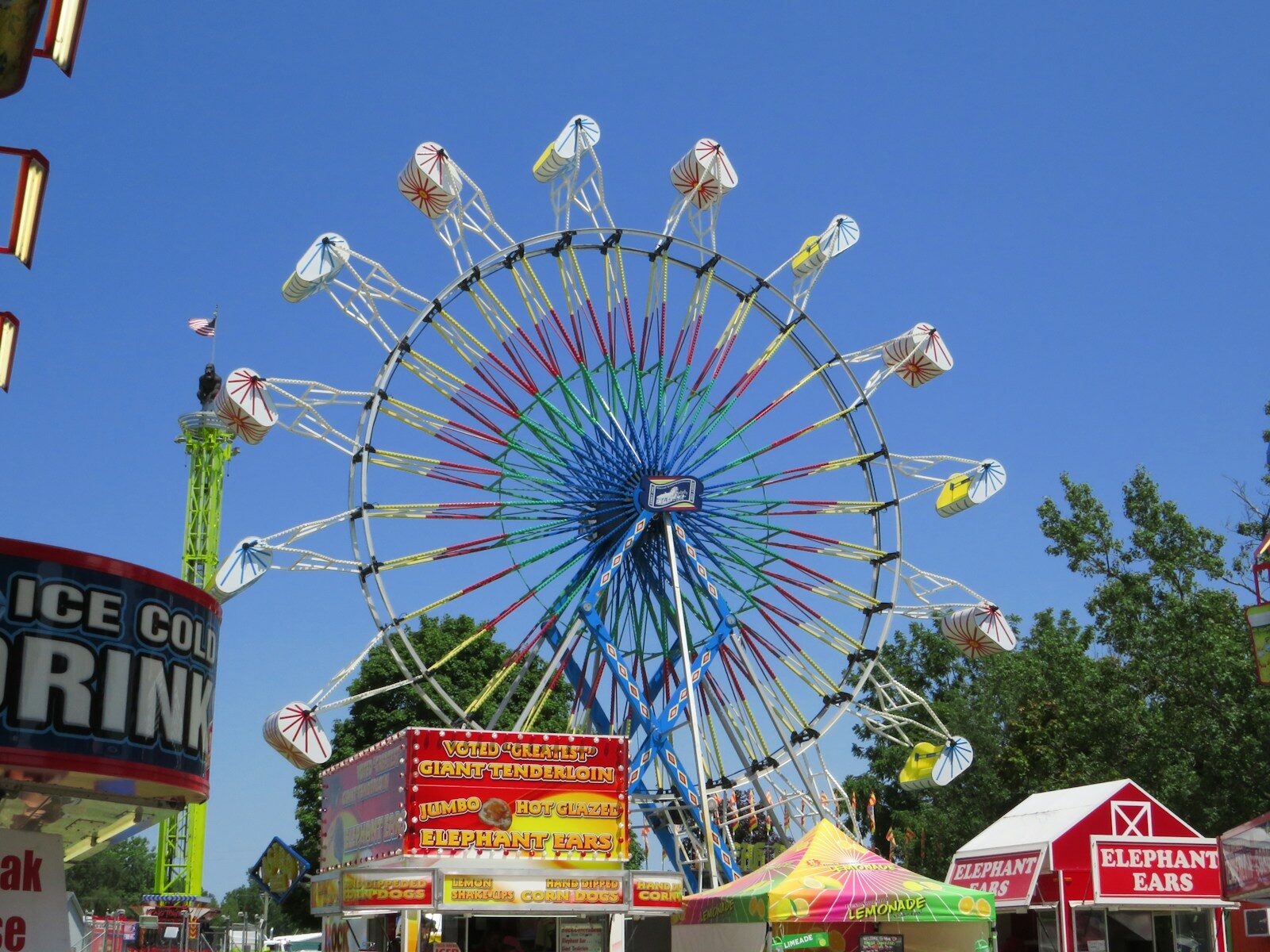A colorful ferris wheel dominates a sunny fairground scene