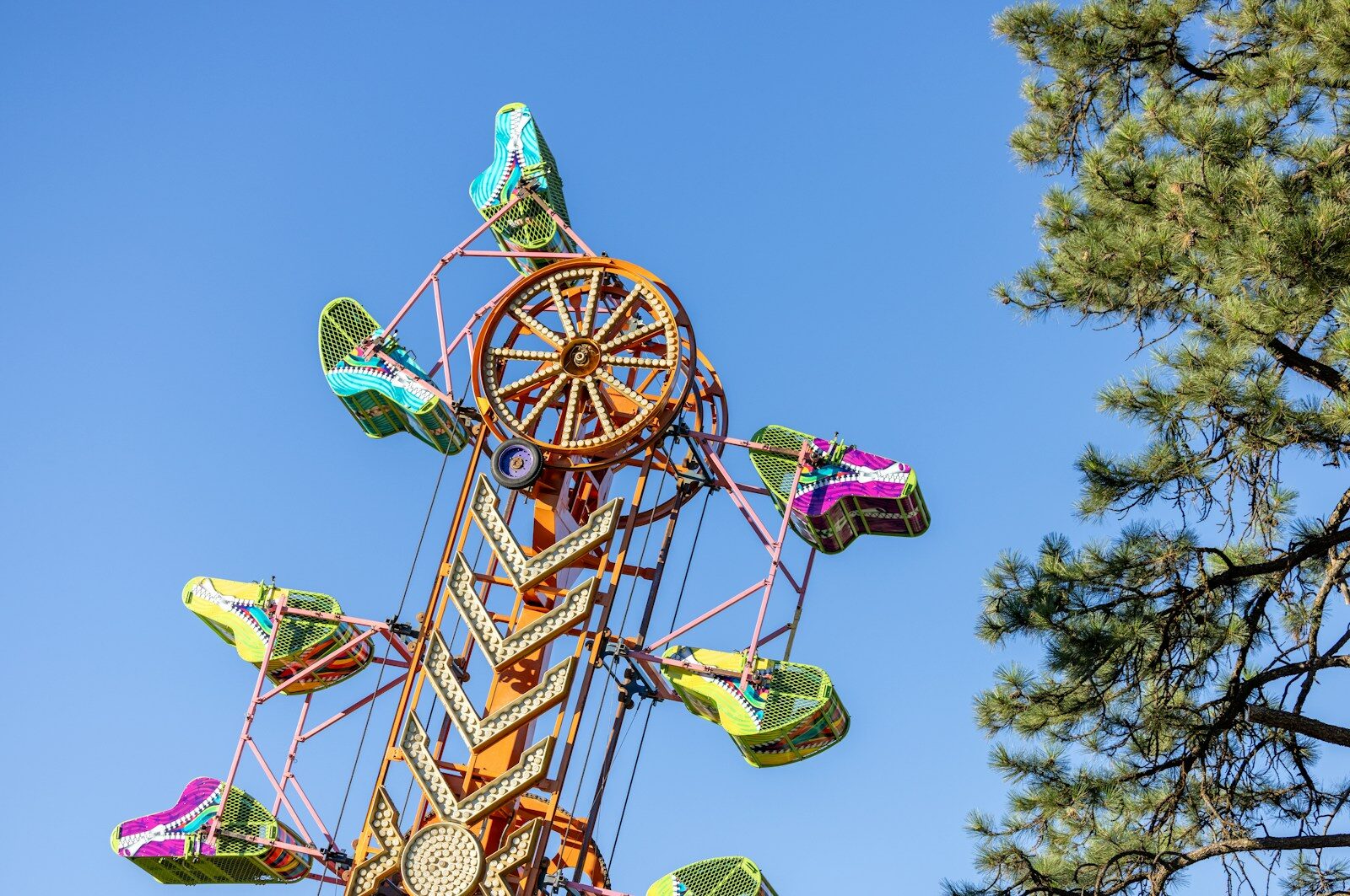 A colorful carnival ride with spinning passenger cars against a clear blue sky