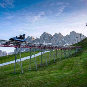 mountain coaster running down a green summer ski slope with snowy peaks in the background